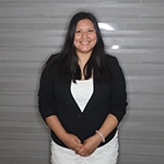A smiling woman wearing a black blazer and white top, standing against a neutral background.