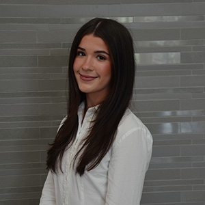 Female with long dark hair, wearing a white shirt and smiling.