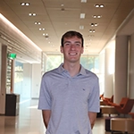 A smiling young man stands in a bright, modern hallway.