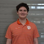 Young man wearing an orange striped Clemson University polo shirt, smiling in an indoor setting.