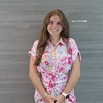 Young woman smiling against a gray wall, wearing a colorful floral shirt.
