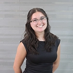 A smiling young woman with long, dark hair wearing glasses and a black top.