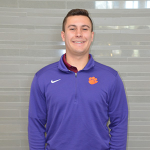 Man with short brown hair smiling and wearing a purple collared pullover.