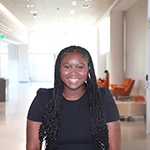 A smiling woman with long braided hair sitting in a modern office environment.