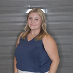 A young woman with blonde hair, wearing a blue top, smiles confidently against a gray background.