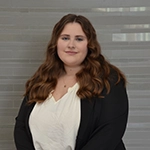 Professional portrait of a woman with long, wavy hair, wearing a white blouse and black blazer, set against a neutral background.