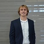A young man in a blazer and white shirt smiling against a modern background.