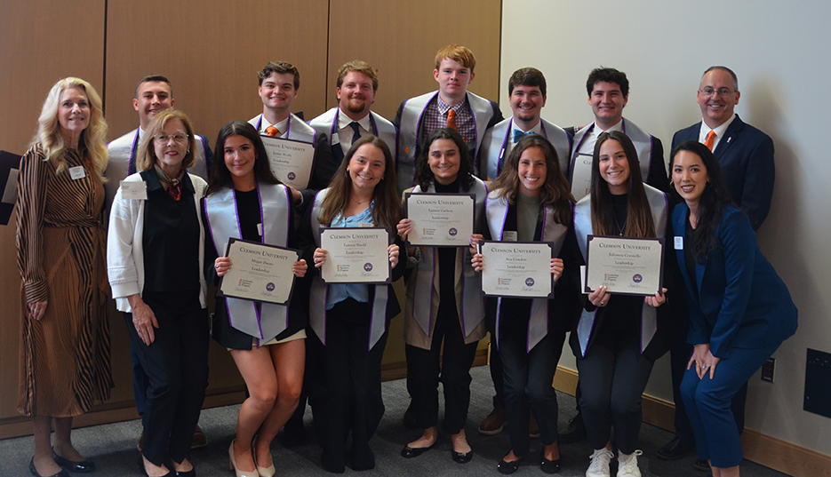 Group photo of graduates holding certificates, posing together with faculty and staff at a graduation ceremony.