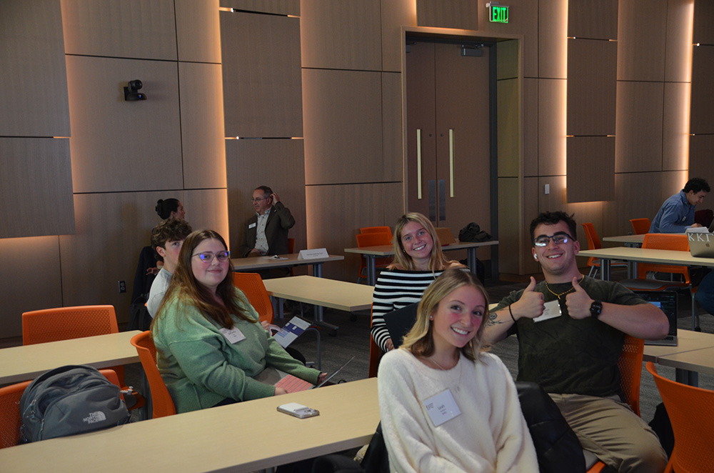 Group of students sitting in a modern classroom, smiling and engaging with the camera.