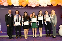 Group of people posing on a stage at an awards ceremony, with several holding certificates.
