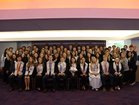 Large group of formally dressed people posing together in several rows on a stage in an auditorium.