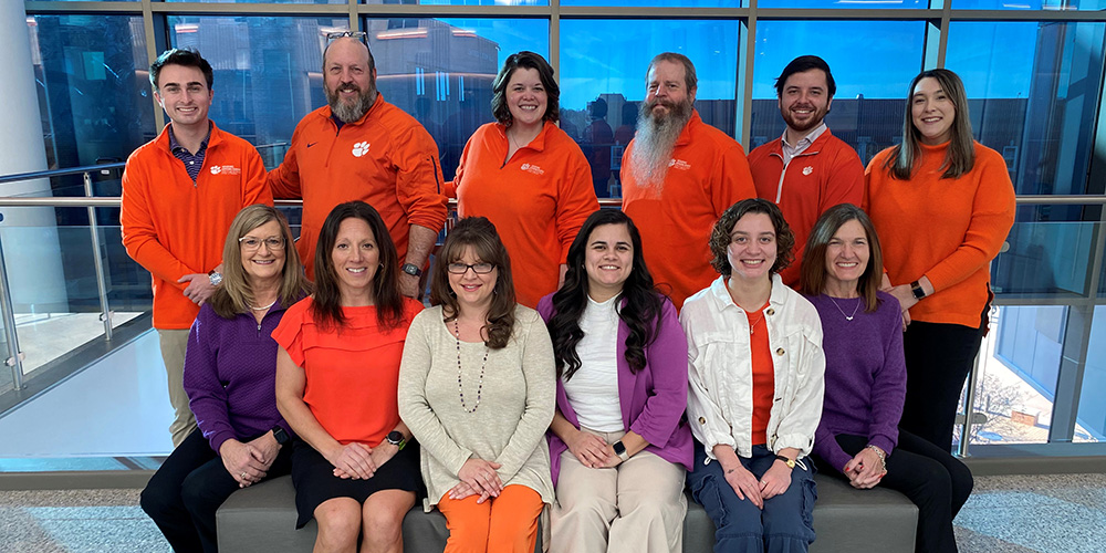 A group photo of staff members wearing Clemson University apparel, showcasing a mix of orange and purple clothing.