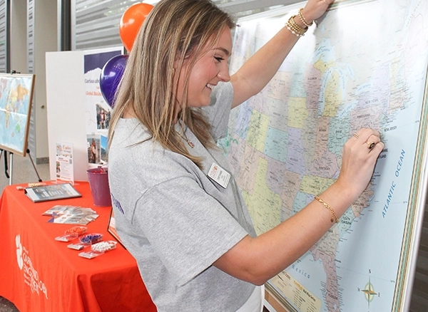 A woman marks a map of the United States while engaging in a workshop, with informational materials and decorations in the background.