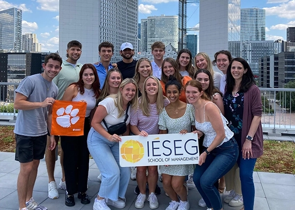Group photo of students from IESEG School of Management holding a university banner and a Clemson flag, set against a cityscape backdrop.