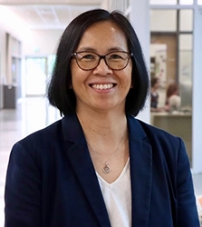 A smiling woman wearing glasses and a blazer in a bright, modern indoor setting.
