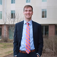 A young man in a suit and tie stands confidently outside a modern building.