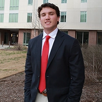 A young man in a business suit and red tie stands confidently outside a modern building.
