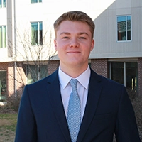 Young man in a suit and tie standing outside a modern building, smiling confidently.