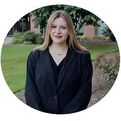 Portrait of a woman in a black blazer standing outdoors on a landscaped campus.