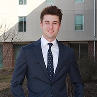 A young man in a suit standing confidently in front of a modern building.