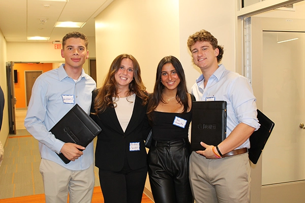A group of four young professionals smiling and posing together, holding folders at a networking event.
