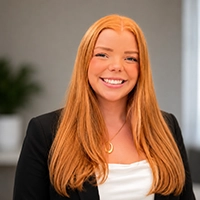 Smiling woman with long red hair wearing a black blazer and white top in an office setting.