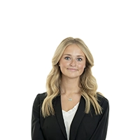 Studio headshot of a blonde woman wearing a black blazer over a light top against a white background.