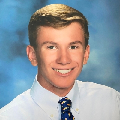 A smiling young man in a collared shirt and patterned tie, set against a blue background.