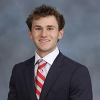 Professional headshot of a young man in a suit and tie with a friendly smile.