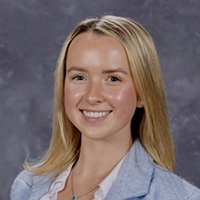 A smiling young woman with long blonde hair, wearing a light blue blazer and a white top.