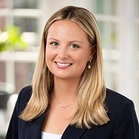 Professional headshot of a smiling woman with blonde hair wearing a dark blazer in a bright indoor setting.