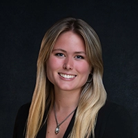 Professional headshot of a young woman with long blonde hair smiling against a dark background.