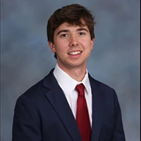 Professional headshot of a young man wearing a dark suit and red tie, with a neutral background.