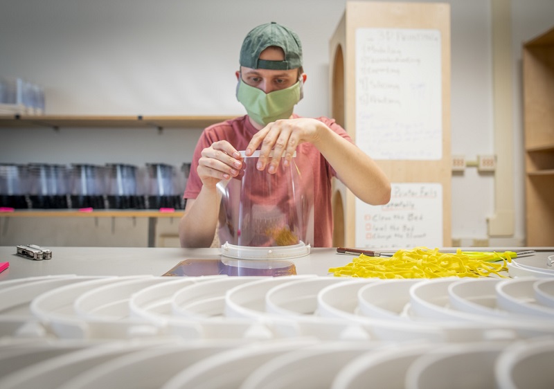 Kevin Crumley, a graduate student from Greenville, S.C. in Clemson University’s architecture program poses with rows of face shield head bands produced with 3D printers by a group of students and recent graduates.