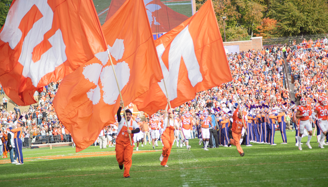 students running with clemson flags at the start of wake forest football game