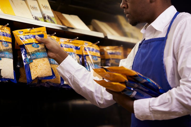 grocery store worker holding a bag of packaged cheese