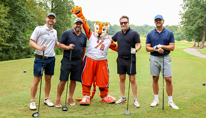 4 people and a tiger mascot posing in a field
