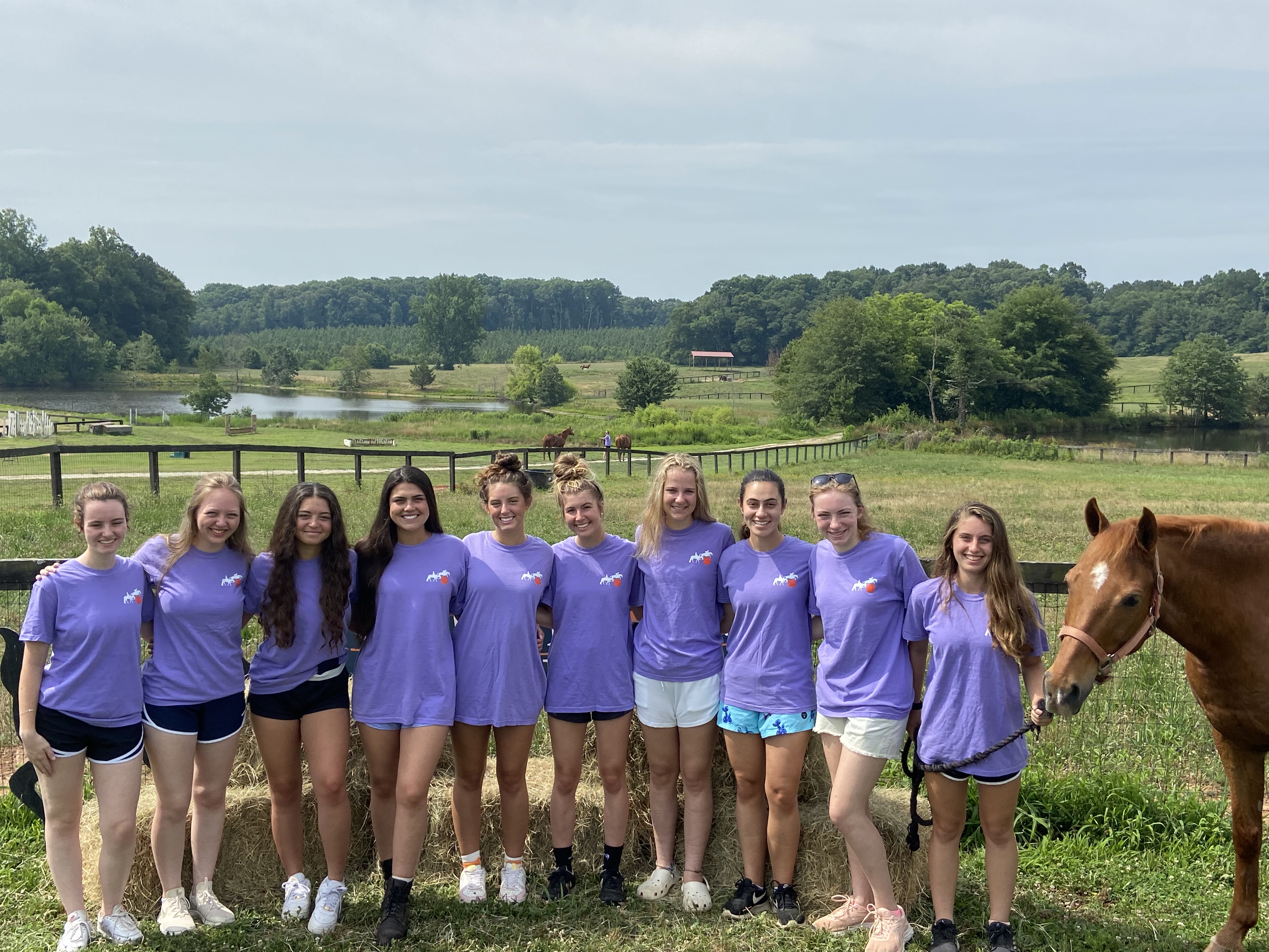 group photo of camp participants in a field standing with a horse