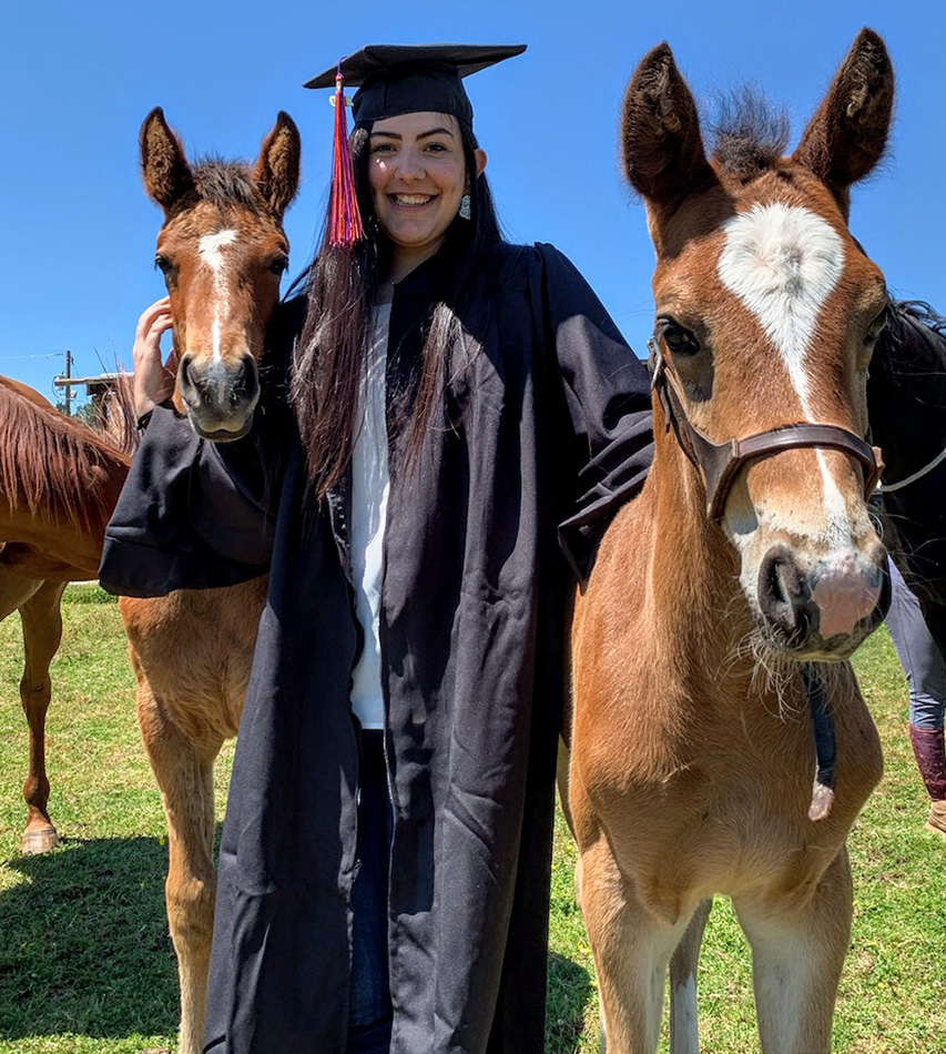 kendall in cap and gown smiling with two foals