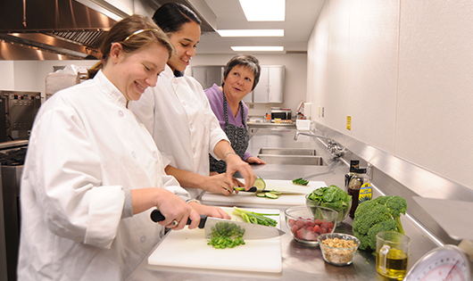 Students slice vegetables while Dr. Marge Condrasky looks on.