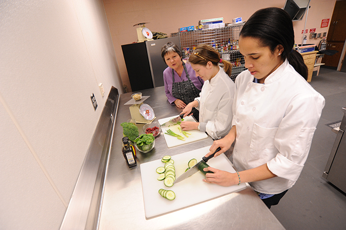 two female students slice vegetables while Dr. Marge Condrasky looks on.