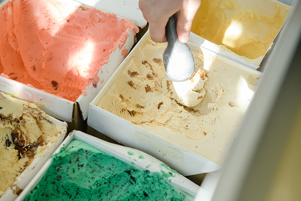 An ice cream scoop scooping ice cream out of a collection of ice cream containers