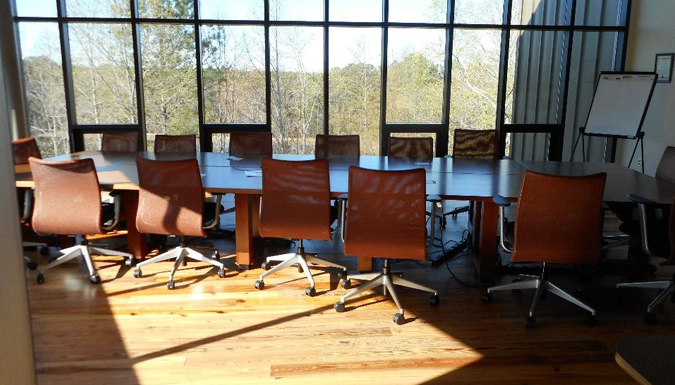 conference room with large table and chairs around, near a wall of windows overlooking treetops