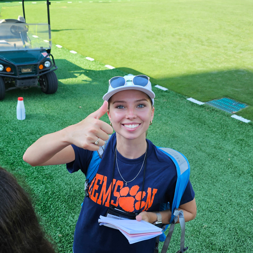 young feaml student in a clemson t shirt standing on the football field  showing a thumbs up