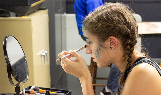 Student applies stage makeup in front of mirror