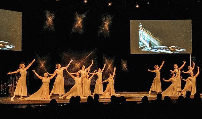 Dancers perform on stage with stained glass projection in backgroun