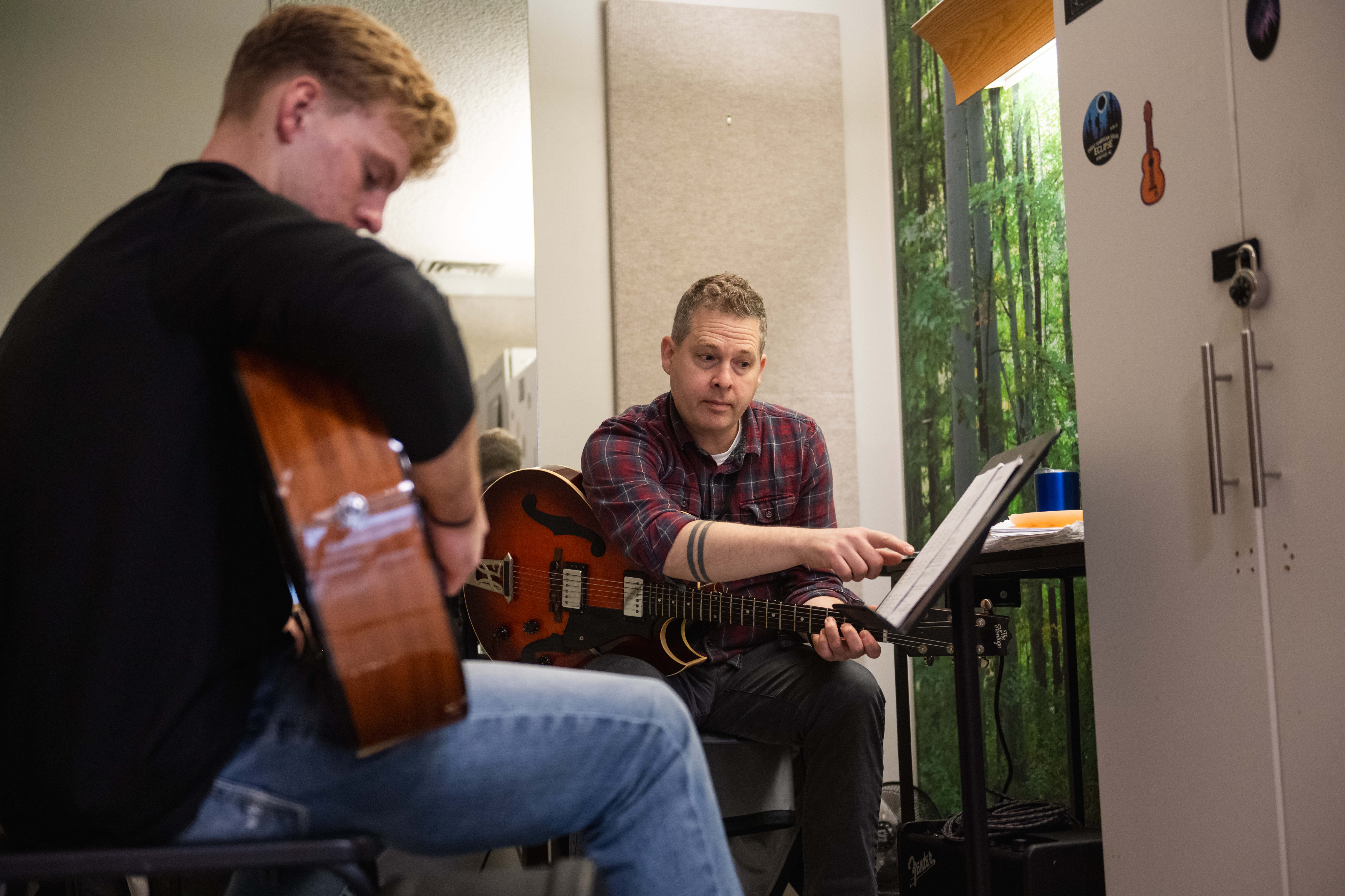 A man teaches guitar to a student inside a lesson room
