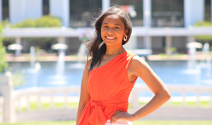 Delaney Toomer smiles in an orange outfit on campus