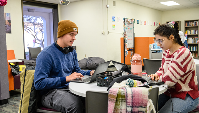 Two students seated at a table with laptops
