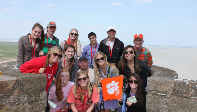 A group of people stand near the ocean holding a Clemson flag